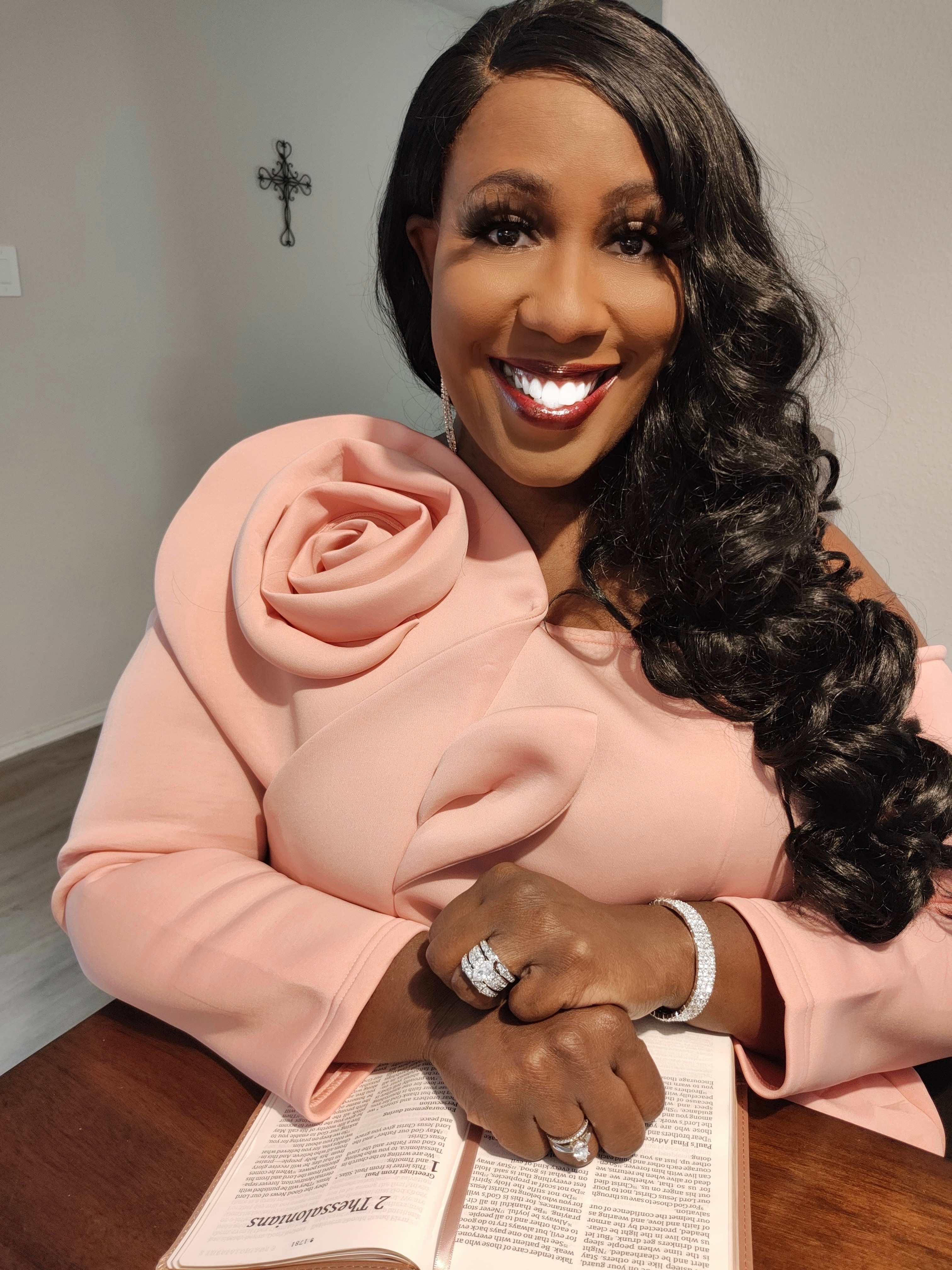 Shamarian Smith Love smiling in a pink dress with her hands in prayer on top of The Holy Bible